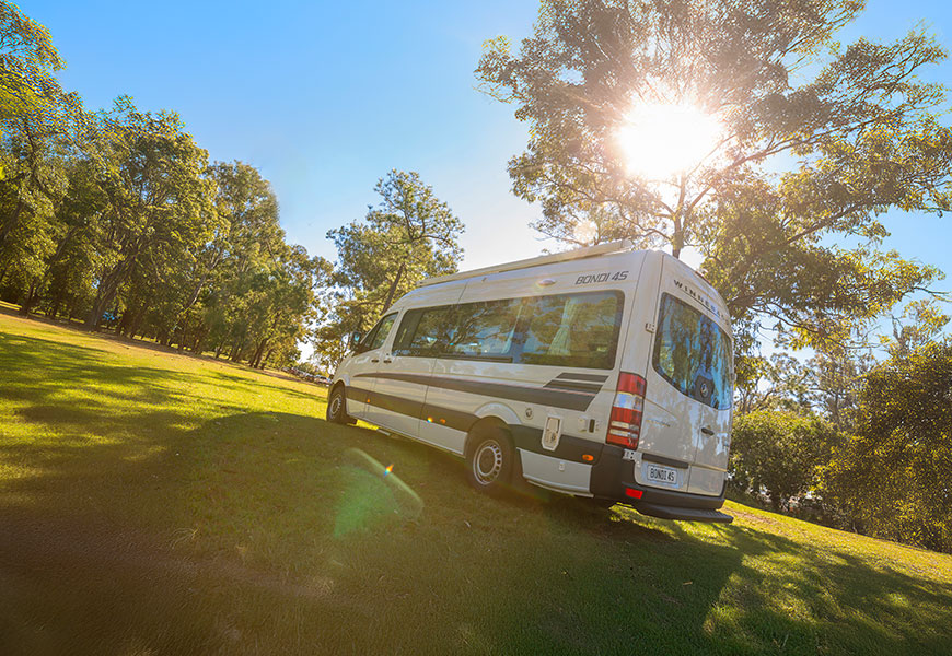 Winnebago campervan parked up on the grass with sun in the background.